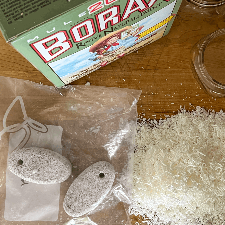 Box of Borax, 2 pumice stones in a bag and a pile of grated bar soap on a wood cutting board.