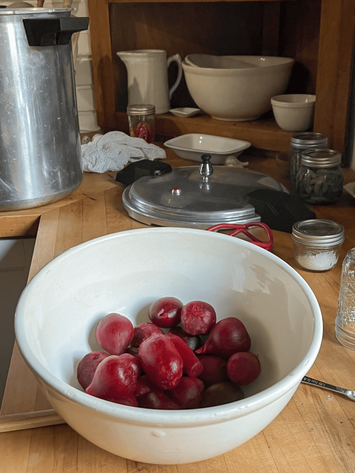 Cooked and peeled red beets in an ironstone bowl on a wood counter with pressure cooker in behind.