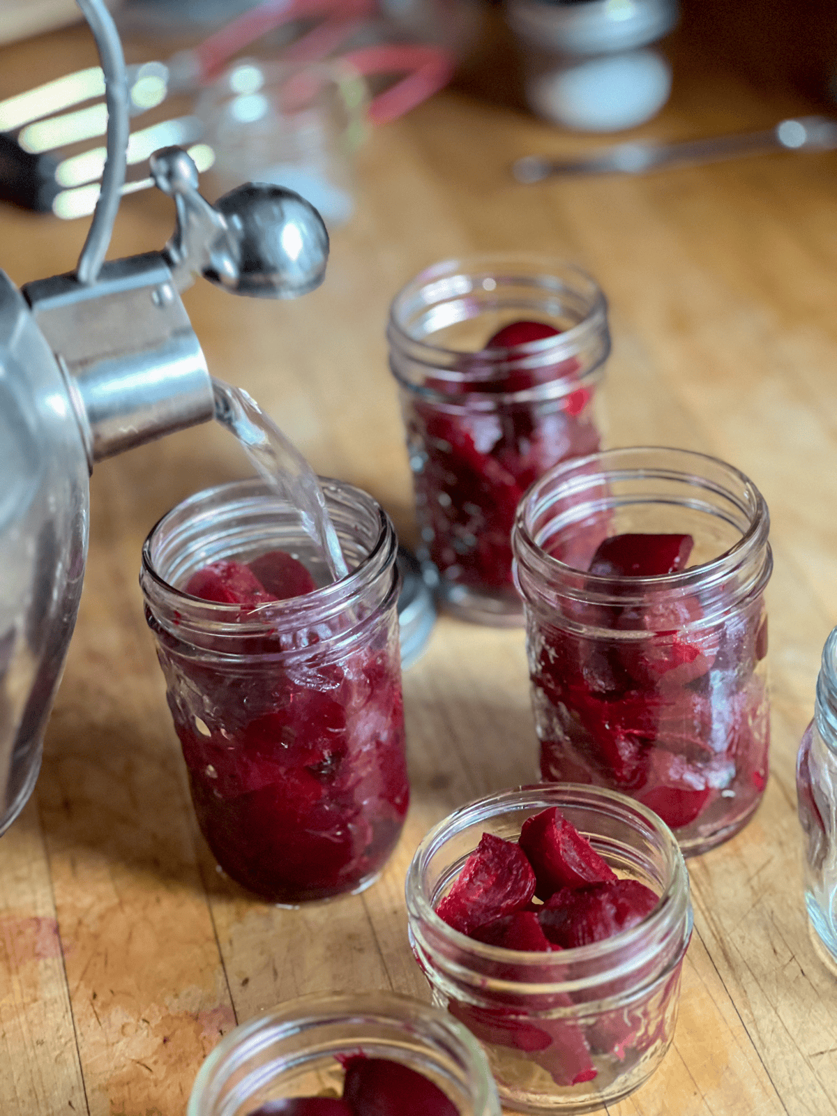 Adding boiling water from a kettle to mason jars full of beets for canning.