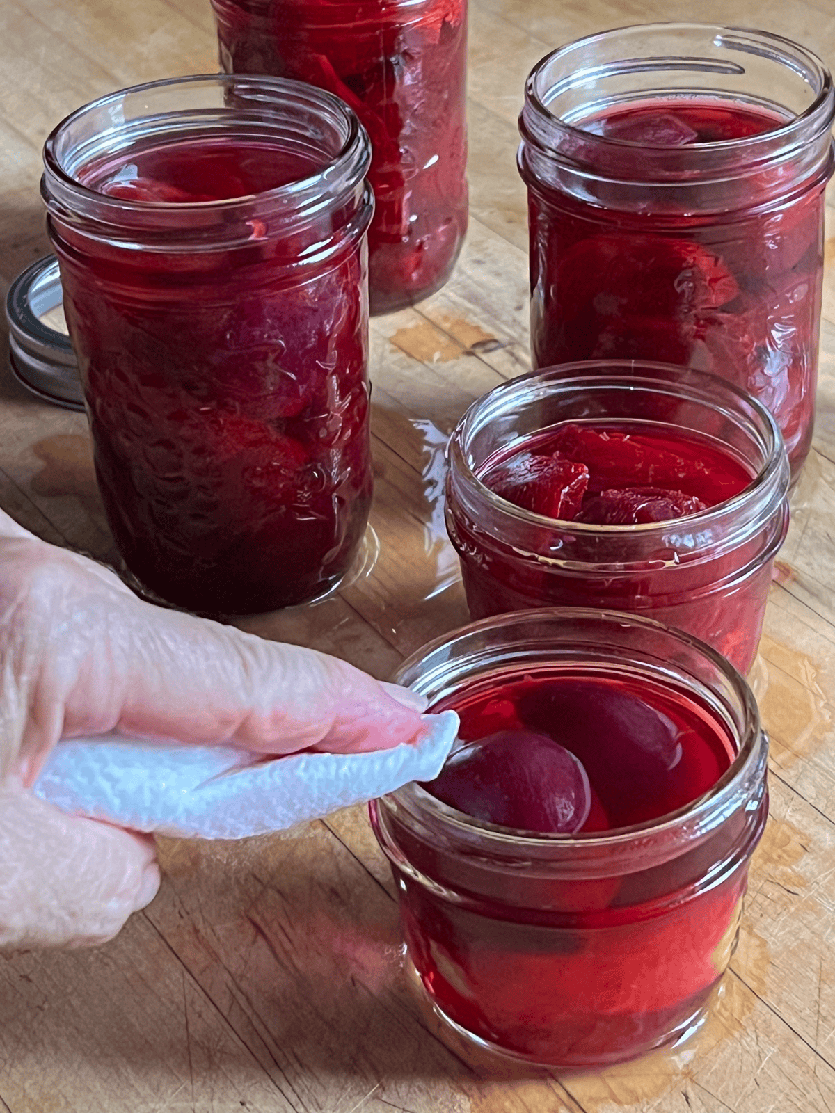 Fingertip wipes the rim of a mason jar filled with beets to be processed.