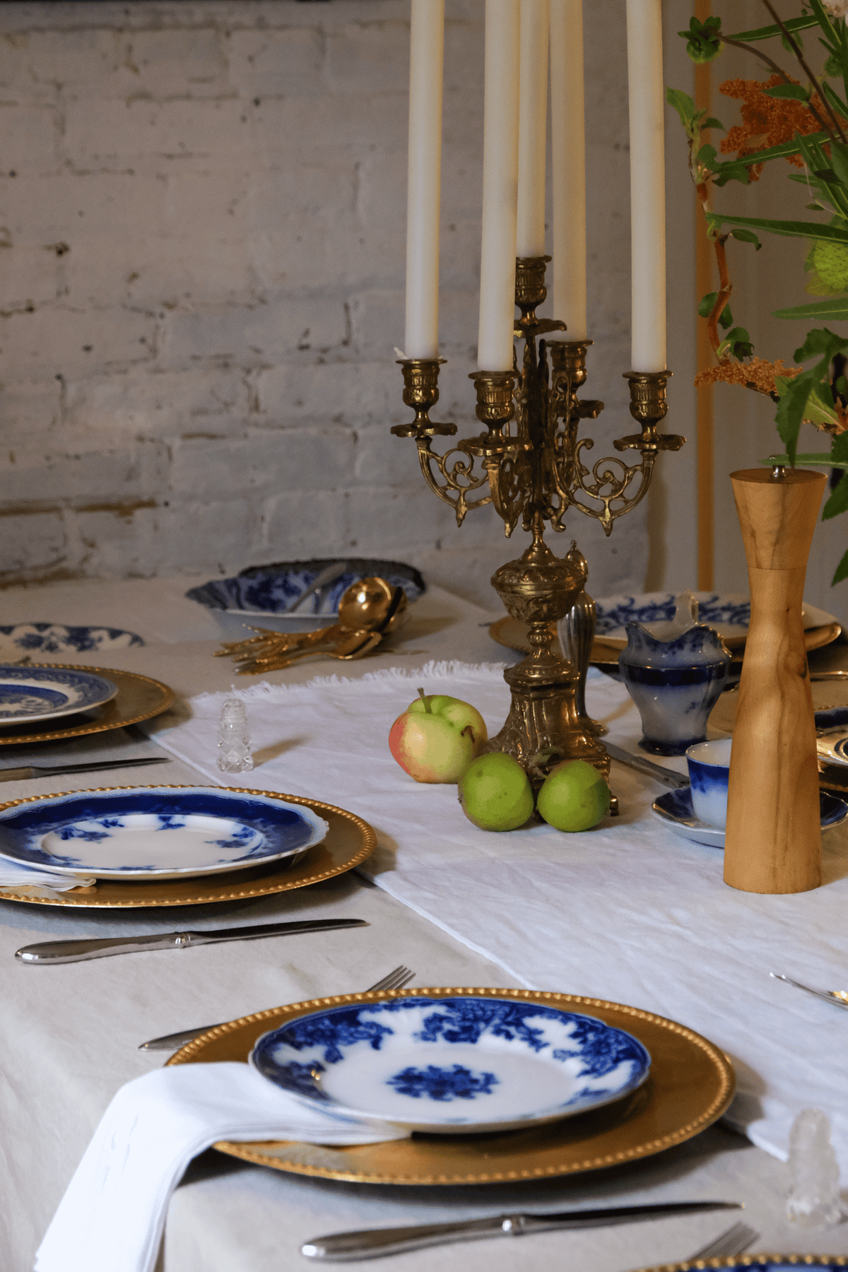 Dining room harvest table set with linen, antique flow blue dishes, gold chargers.