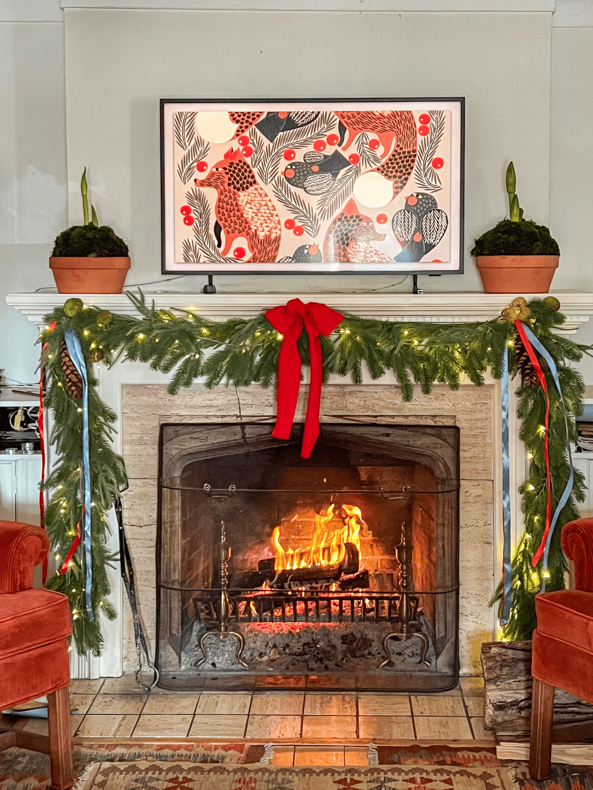 Frame TV on a fireplace mantle flanked with 2 clay pots mounded with moss and amaryllis bulbs.