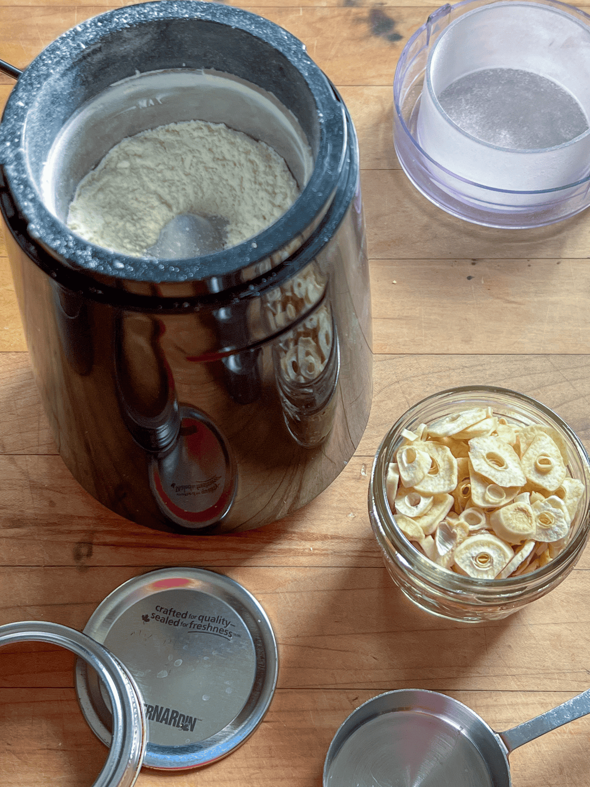 Slices of dried garlic in a mason jar beside a coffee grinder filled with newly ground garlic powder.